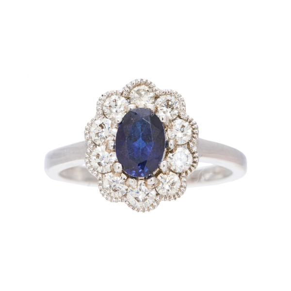 Sortija rosetón en oro blanco con zafiro azul talla oval orlado por diamantes talla brillante.