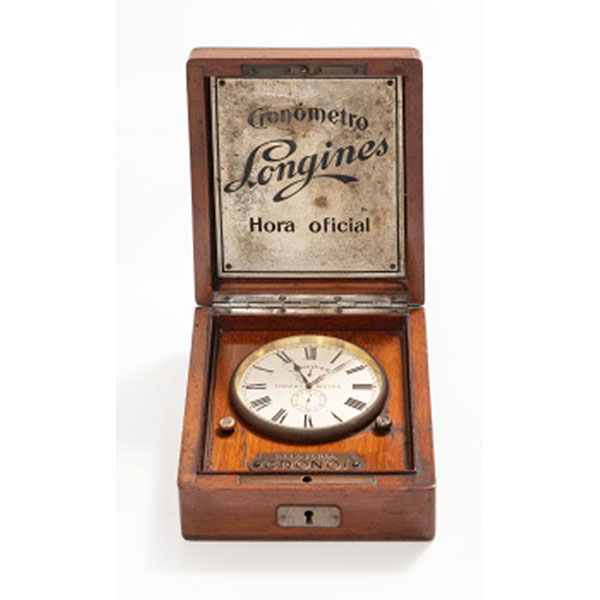 Reloj de sobremesa marca Longines cronómetro, hora oficial, esfera con números romanos y bisel en metal. Caja en madera de caoba. Relojería Cronos Joyería.
