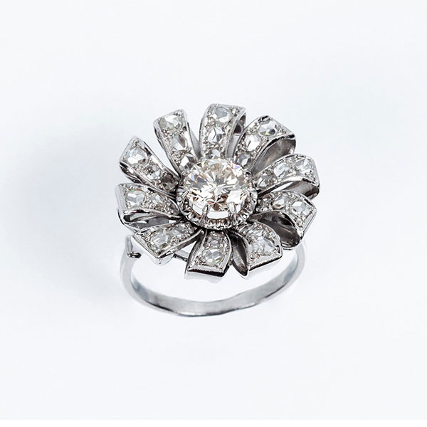 Bella sortija vintage en forma de flor, en platino, con un limpio y blanco diamante central, talla brillante orlado en &#039;pétalos&#039; cuajados de diamantitos 