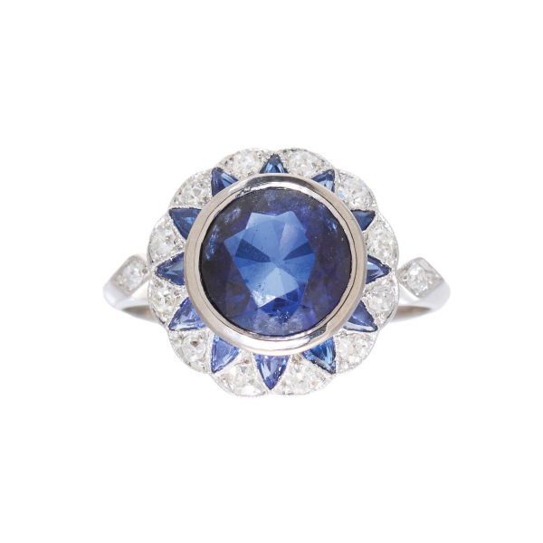 Sortija en oro blanco con zafiros azules tallas redonda y triángulo y orla de diamantes talla brillante antigua.