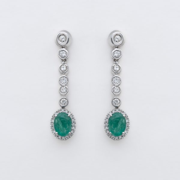 Pendientes largos en oro blanco con l&iacute;nea y roset&oacute;n de diamantes talla brillante y esmeralda talla oval engastados en garras y chat&oacute;n.