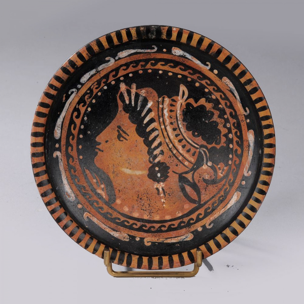 Plato sobre pedestal ligero decorado con un rostro de perfil rodeado de varios frisos. Diámetro 13 cm.
