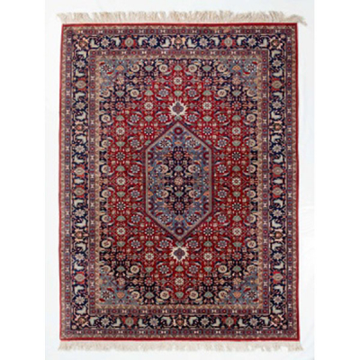 Alfombra de lana con medallón central y greca alrededor con decoración geométrica y vegetal en tonos granates, azules y beiges.