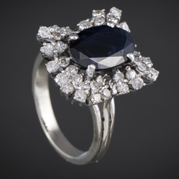 Anillo en oro blanco de 18 kt con zafiro central orlado de brillantes.