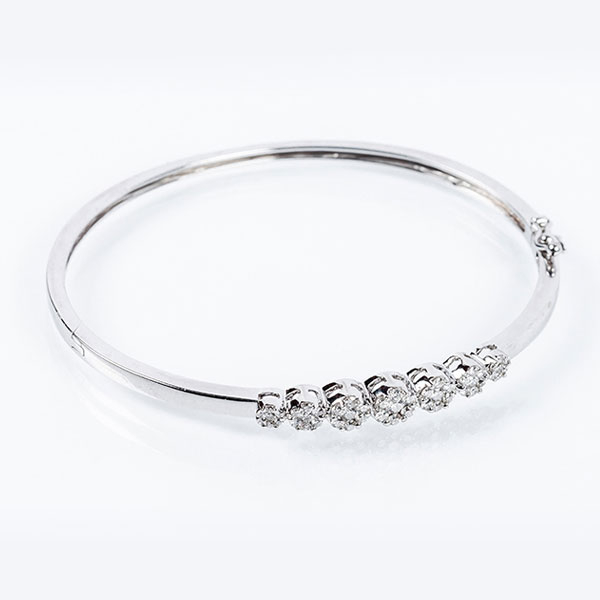 Brazalete esclavo en s&oacute;lida montura de oro blanco 18 K, con motivo central de siete rosetones de limpios y blancos diamantes naturales 