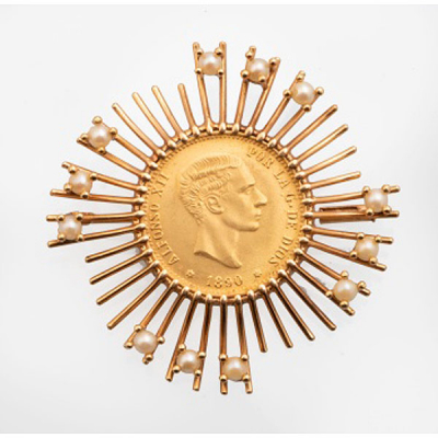 Broche en oro amarillo en forma de sol con decoración de moneda central y perlas.