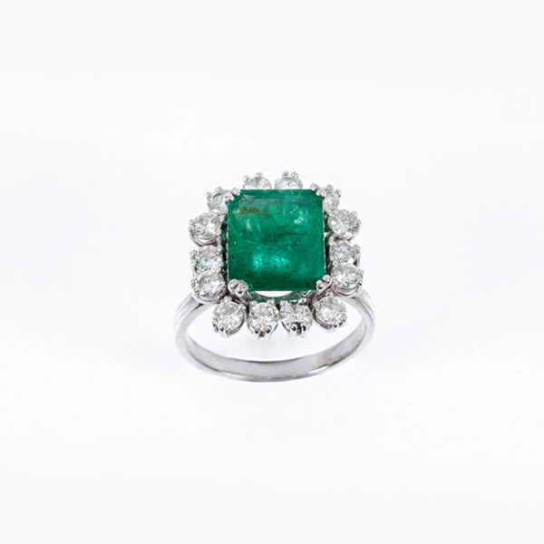 Sortija en oro blanco 18 K con una gran esmeralda de intenso color, en su talla, orlada de limpios y blancos diamantes 