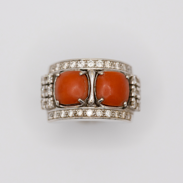 Sortija en oro blanco con dos cabujones de coral engastados en garras y ornamentada con diamantes talla brillante.