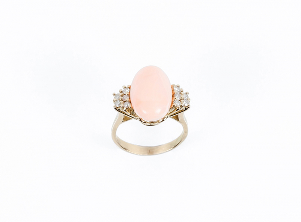Sortija en oro amarillo con centro en cabujón de coral rosa, entre filas de limpios y blancos diamantes talla brillante, en garras