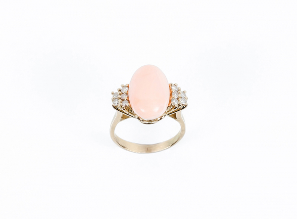 Sortija en oro amarillo con centro en cabujón de coral rosa, entre filas de limpios y blancos diamantes talla brillante, en garras