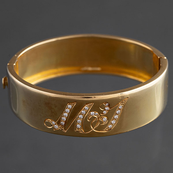 Brazalete rígido en oro amarillo de 18kt con dos iniciales cuajadas de brillantes.