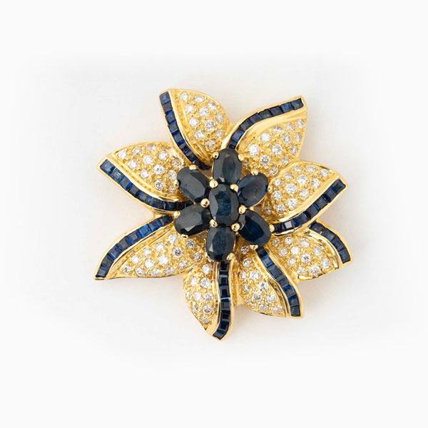 Alfiler en sólida montura de oro amarillo 18 K, en forma de estrella, con centro en flor formada por zafiros finos azules, talla oval