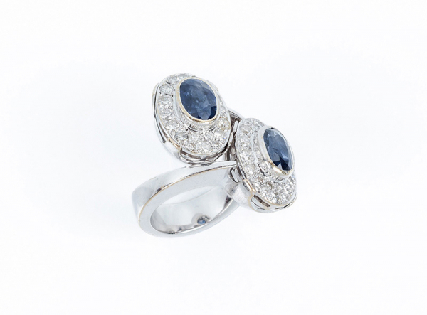 Sortija 'tú y yo' en montura maciza de oro amarillo rodiado, con dos rosetones con centro de zafiro fino azul, oval, y orla cuajada de limpios y blancos diamantes talla brillante