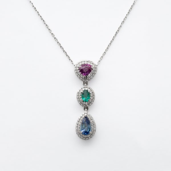 Gargantilla en oro blanco con tres rosetones de rubí talla trillón, esmeralda talla oval y zafiro azul talla perilla orlados por dos bandas de diamantes talla brillante.
