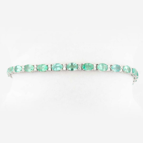 Pulsera riviere en oro blanco 18 K con fila de bonitas esmeraldas naturales, talla oval, en garritas, intercaladas con pares de limpios y blancos diamantes, talla brillante