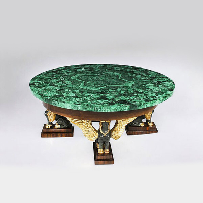 Importante mesa de centro con base sujeta por cuatro esfinges en madera de nogal tallada y con tapa redonda de malaquita, Francia, siglo XX.