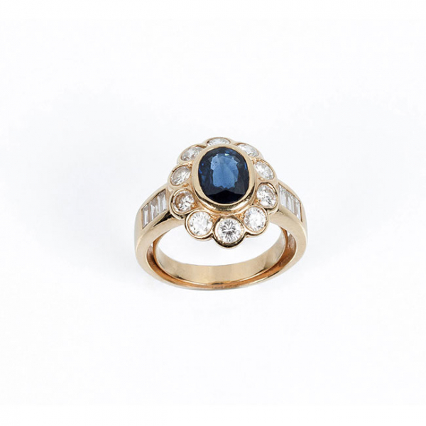 Sortija en sólida montura de oro amarillo 18 K con zafiro fino azul, oval, en chatón, y orla en fila de limpios y blancos diamantes, 