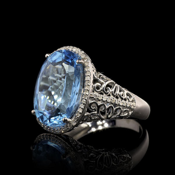 Anillo de oro blanco 18K con topacio oval y diamantes talla brillante, con cenefa tallada con flor de lis. 