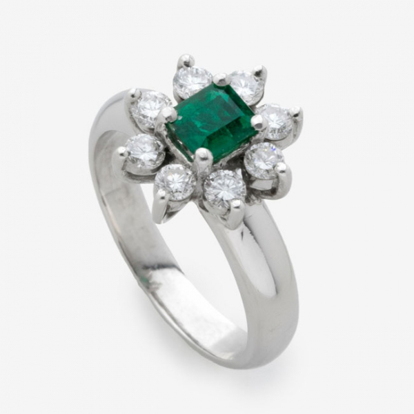 Sortija en oro blanco con esmeralda central y diamantes talla brillante alrededor formando flor con un peso total de 0,24 cts.