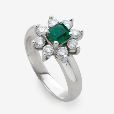 Sortija en oro blanco con esmeralda central y diamantes talla brillante alrededor formando flor con un peso total de 0,24 cts.