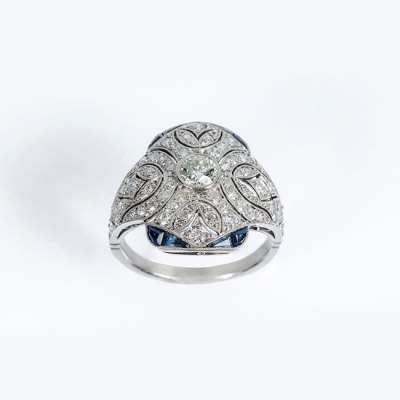Delicada sortija estilo art-decó en platino, con un limpio y blanco diamante, talla brillante central con diamantitos y zafiros finos azules 