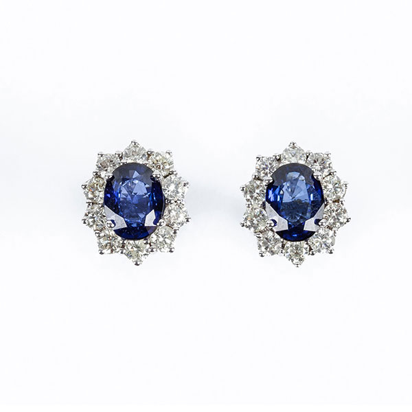 Pendientes en oro blanco con un bonito zafiro fino azul oval y orla de limpios y blancos diamantes, talla brillante, en garras