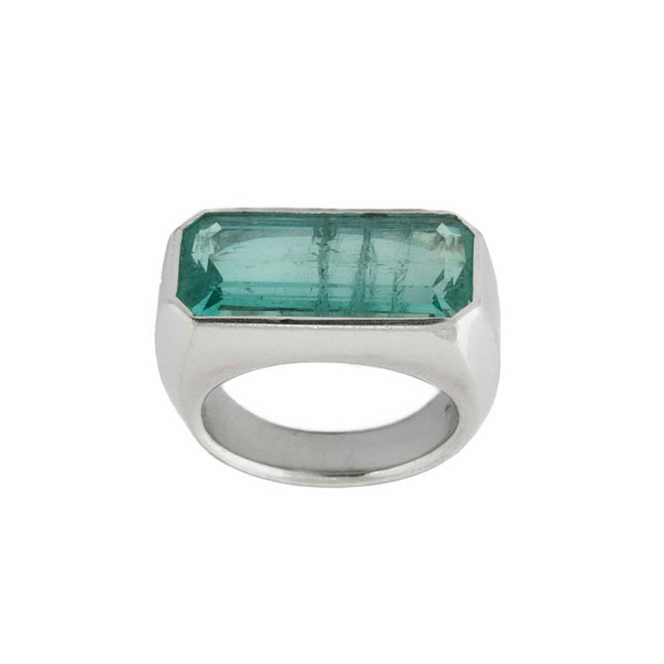 Anillo en montura maciza de oro blanco 18 K con una turmalina natural, verde-azulada, rectangular, dispuesta transversalmente.