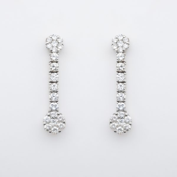 Pendientes largos en oro blanco con dos rosetones unidos por l&iacute;nea de diamantes talla brillante.