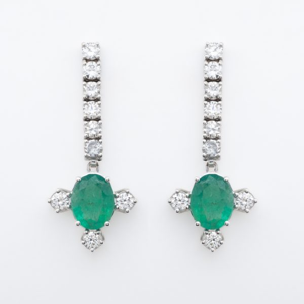 Pendientes largos en oro blanco con tira de diamantes talla brillante rematada por esmeralda talla oval flanqueada por tres diamantes.