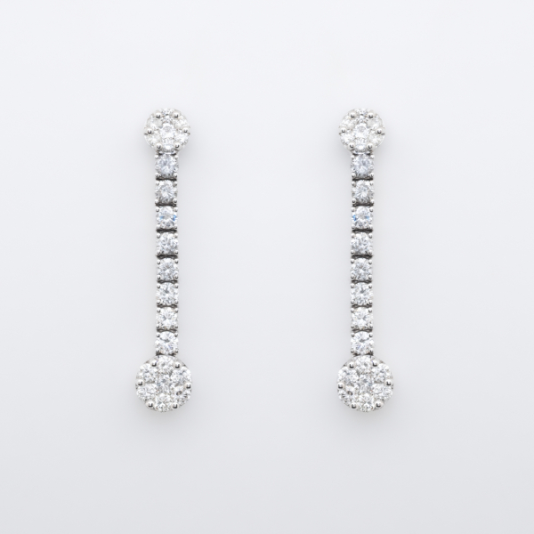 Pendientes largos en oro blanco con dos rosetones unidos por línea de diamantes talla brillante.
