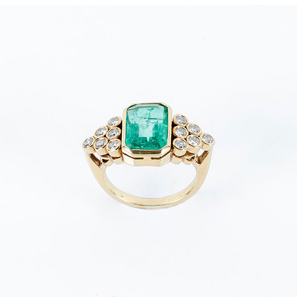 Sortija en oro amarillo 18 K con una bella esmeralda colombiana, en su talla, en chatón, entre motivos triangulares, cuajados de limpios y blancos de diamantes talla brillante 