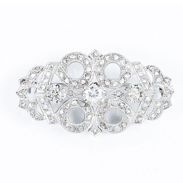 Delicado alfiler vintage en montura calada de platino u oro blanco 18 K, con tres centros de diamante, talla brillante, en garras de ilusión, cuajados de diamantes talla simple 