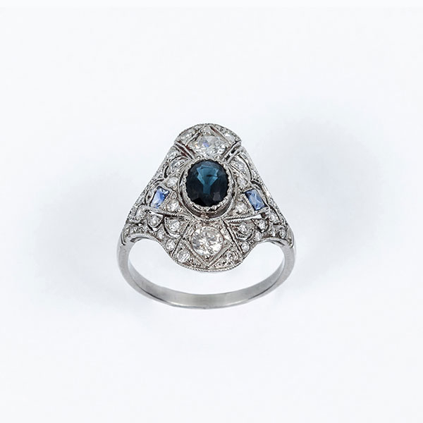 Bella sortija lanzadera estilo 'art-déco'en montura de platino, con centro de zafiro fino azul, oval, sobre motivo calado, cuajado de limpios y blancos diamantes talla brillante y un zafiro 'carré' a cada lado 