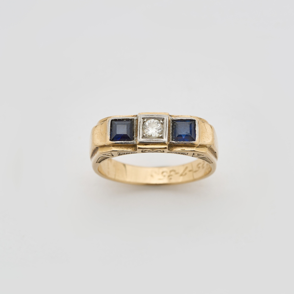 Sortija tresillo en oro y vistas en platino con diamante talla brillante antigua custodiado por símiles de zafiro azul talla carré. 
