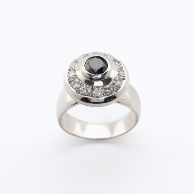 Sortija dise&ntilde;o circular en oro blanco con un diamante negro talla brillante orlado por diamantes talla brillante.
