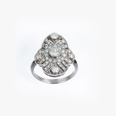 Bella sortija lanzadera art-dec&oacute; en platino cuajada de limpios y blancos diamantes, talla brillante y 8/8. Tiene un brillante central y cuatro centros perif&eacute;ricos en chat&oacute;n, sobre patr&oacute;n calado, oval, en decoraci&oacute;n grafilada