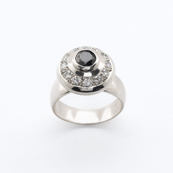 Sortija dise&ntilde;o circular en oro blanco con un diamante negro talla brillante orlado por diamantes talla brillante.