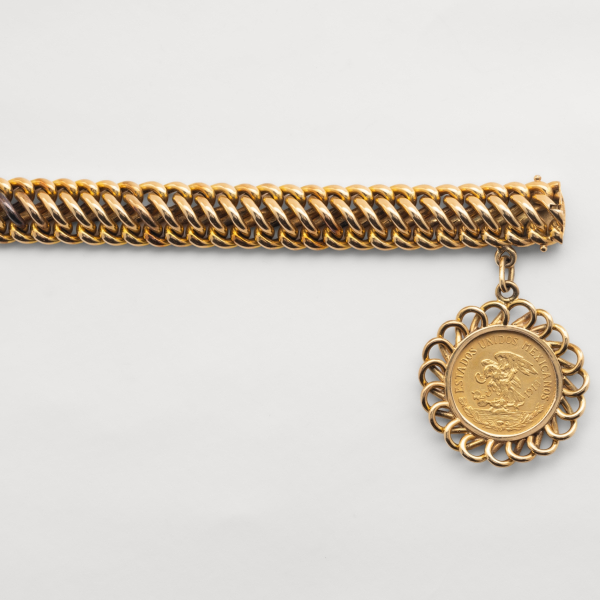 Pulsera semirr&iacute;gida calada con eslabones centrales abobedados que unen los eslabones laterales. Va unida a la pulsera una moneda de 20 pesos mejicanos engarzada en un bisel de eslabones calados entrelazados