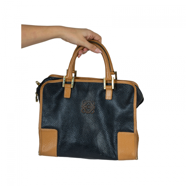 LOEWE. Bolso de mano modelo &laquo;Amazona&raquo; en piel de tonalidad negra y marr&oacute;n camel con logotipo grabado en relieve y cierre de cremallera. Presenta desgastes por uso.