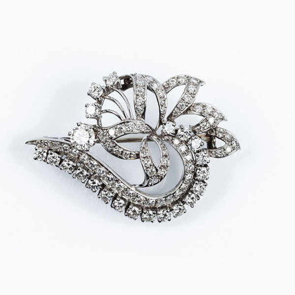 Alfiler-broche vintage en oro blanco, de excelente factura, en diseño floral con lazo, calado, cuajado de limpios y blancos diamantes, talla talla brillante moderna, destacando un brillante central en garras