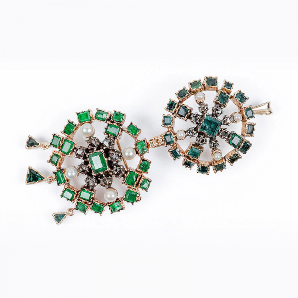 Conjunto desmontable de dos alfileres - colgantes, en rosetón calado cuajado de esmeraldas finas, con centro orlado de diamantes en vistas de plata, y perlitas