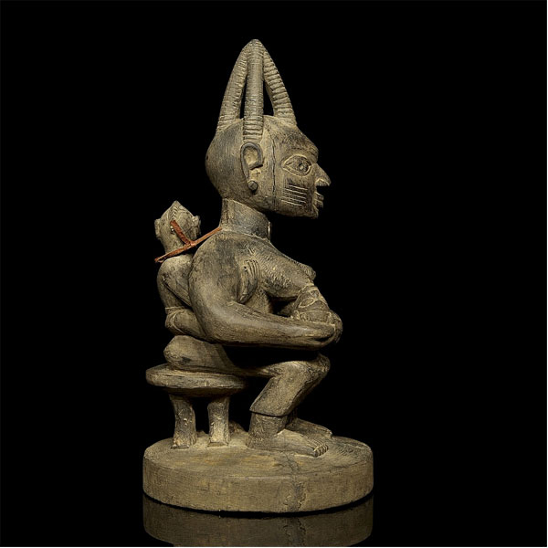 Escultura siguiendo modelos de arte africano. Realizada a partir de madera, en la pieza aparece representada una mujer amamantando a un niño y con un segundo a sus espaldas.