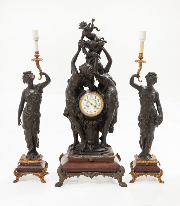 Reloj y pareja de candelabros en calamina patinada con figura representando damas portando candelero dorado con decoración de flores. Estilo Luis XVI. Época Napoleón III. Francia.