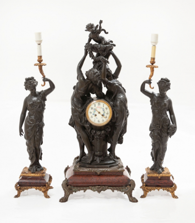 Reloj y pareja de candelabros en calamina patinada con figura representando damas portando candelero dorado con decoración de flores. Estilo Luis XVI. Época Napoleón III. Francia.