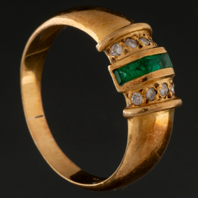 Anillo en oro amarillo de 18 kt con borda de brillantes y banda de esmeraldas calibrados.