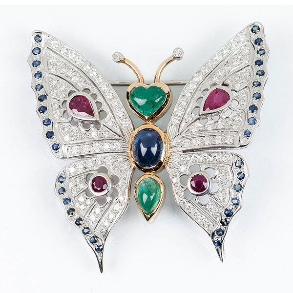 Bello alfiler en montura calada de oro blanco y amarillo 18 K, en forma de mariposa con esmeraldas, zafiros, rubíes y alas cuajadas de limpios y blancos diamantes, talla brillante 