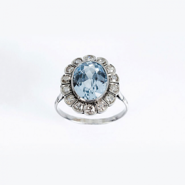 Delicada sortija en platino, con piedra azul, talla oval, orlada de limpios y blancos diamantes 