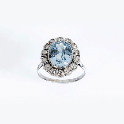 Delicada sortija en platino, con piedra azul, talla oval, orlada de limpios y blancos diamantes 
