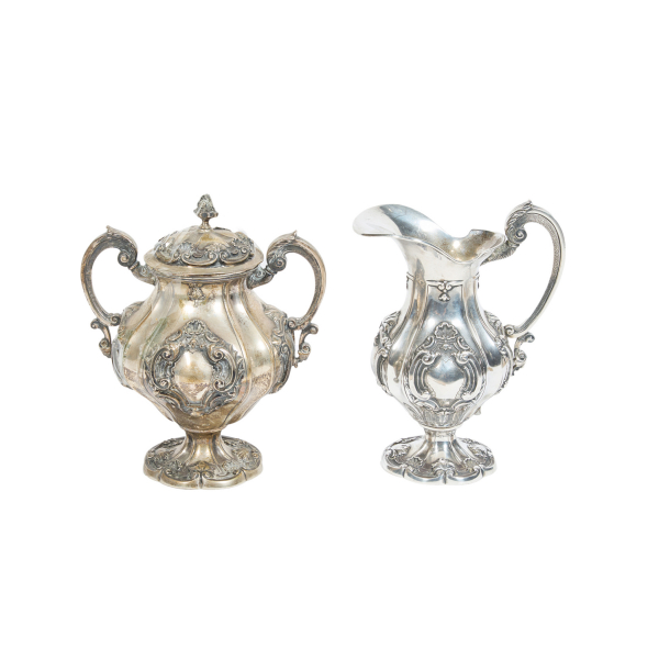 Lote de jarrita y azucarera en plata portuguesa punzonada 800, con decoración repujada de roleos, acantos y motivos vegetales, s.XX.